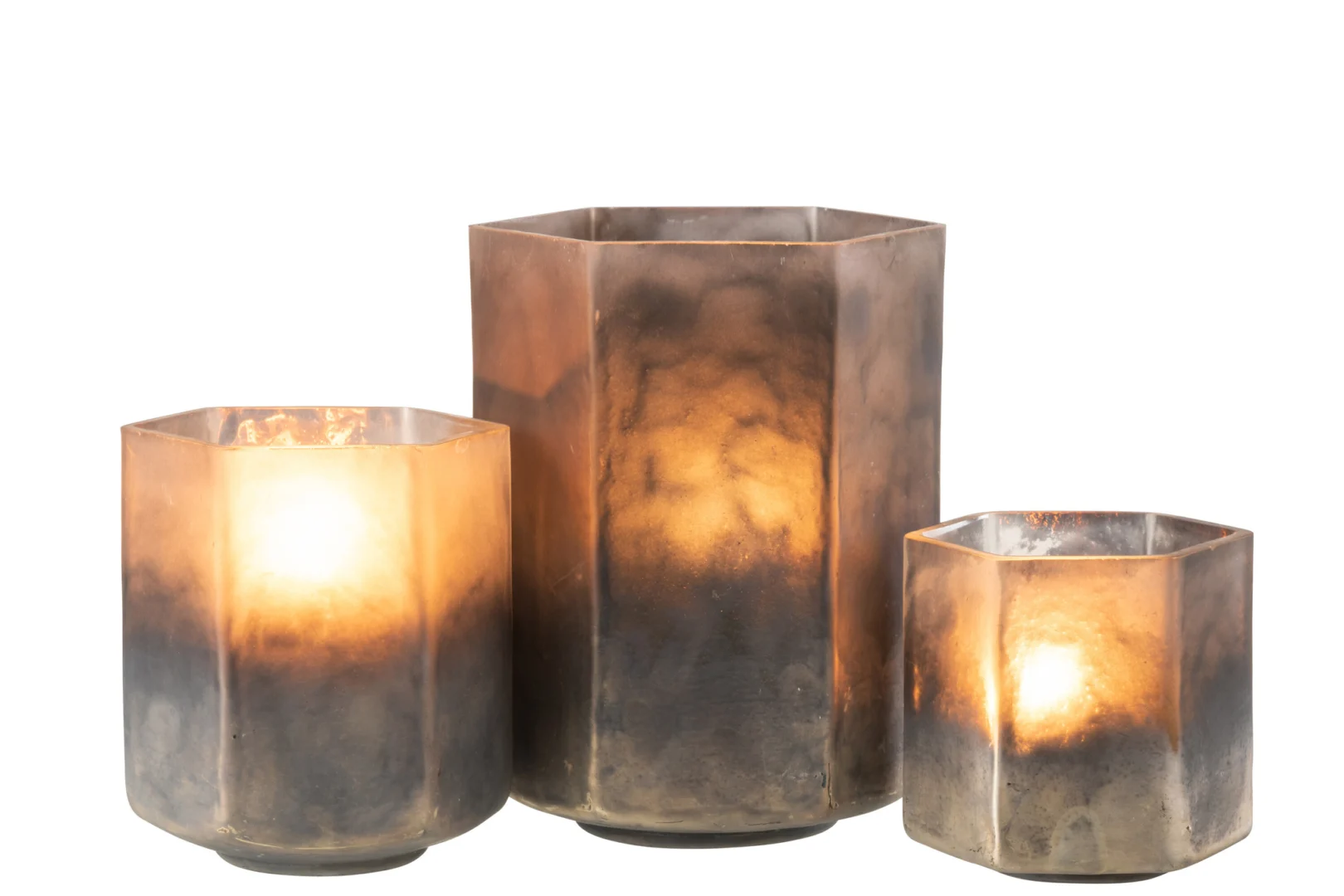 De Kaarsenhouder Orkaan Hexagoon Glas Grijs Groot is een grote, zeshoekige kandelaar van grijs glas met een rokerige afwerking, die een warme gloed afgeeft als hij brandt en mooi afsteekt tegen een witte achtergrond.