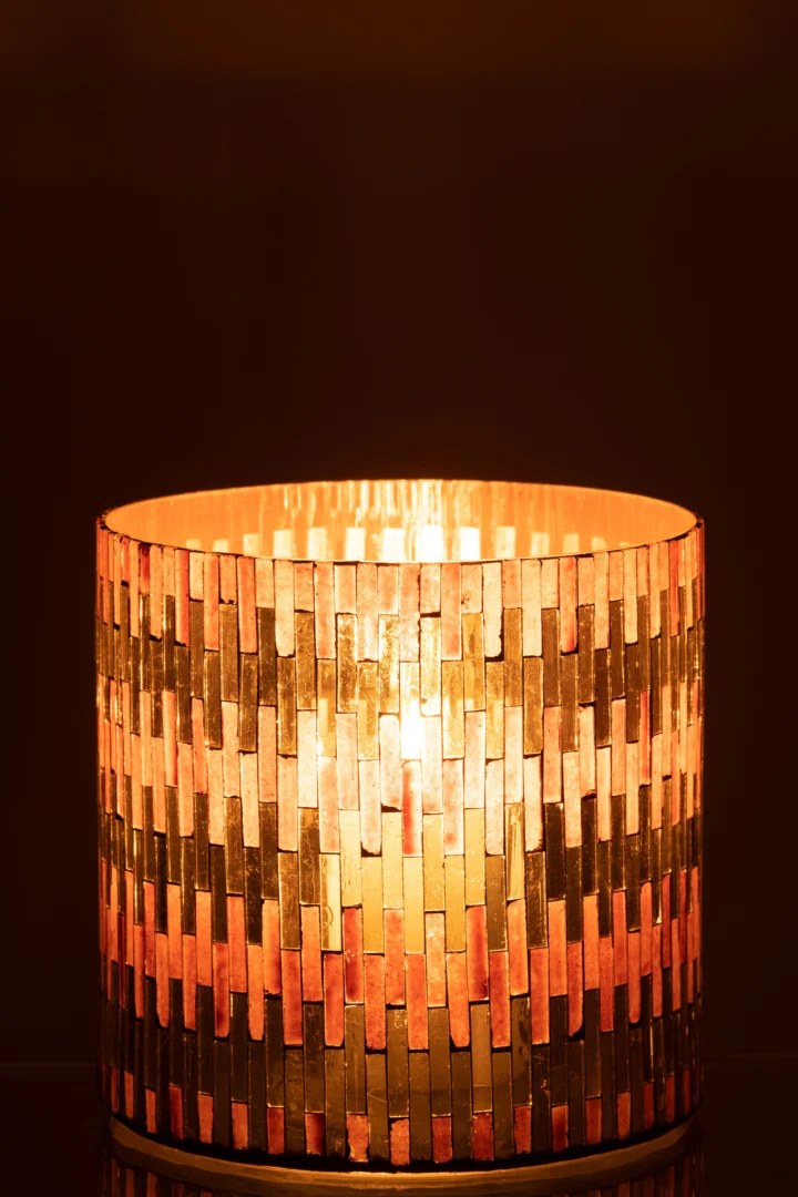 De Kaarsenhouder Orkaan Chic Glas Bruin Goud Groot is een cilindervormige glazen kandelaar met een mozaïek van verticale gouden en bruine tegeltjes, die een warme gloed uitstralen tegen een donkere achtergrond.