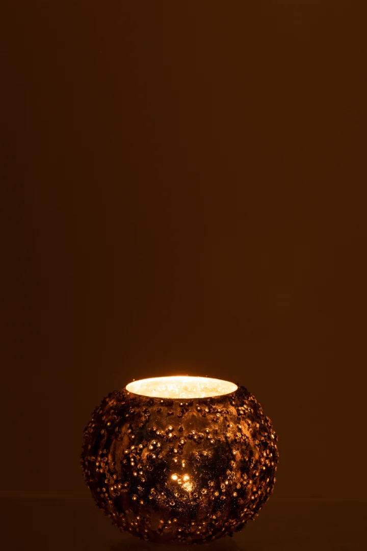 De Theelichthouder Lise Glas Bruin Goud Klein straalt warm in de ronde houder met textuur en werpt een gezellig licht tegen een donkerbruine achtergrond.