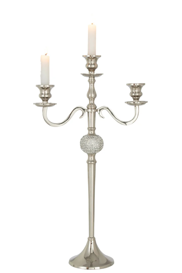 De Kandelaar Op Voet Diamant Bol Aluminium Zilver is een zilveren kandelaar met drie armen, voorzien van een decoratief diamantvormig kristalaccent en met links en in het midden twee witte brandende kaarsen, waarbij de rechter houder leeg is.
