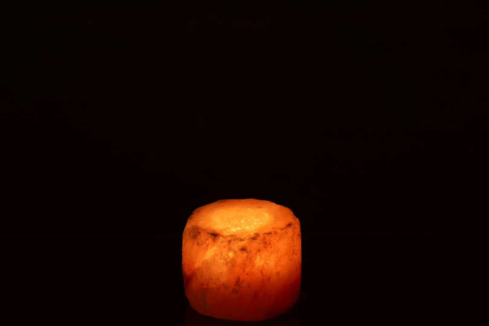 De Theelichthouder Oranje Rotszout gloeit zacht tegen een donkere achtergrond en werpt een warm en rustgevend licht.