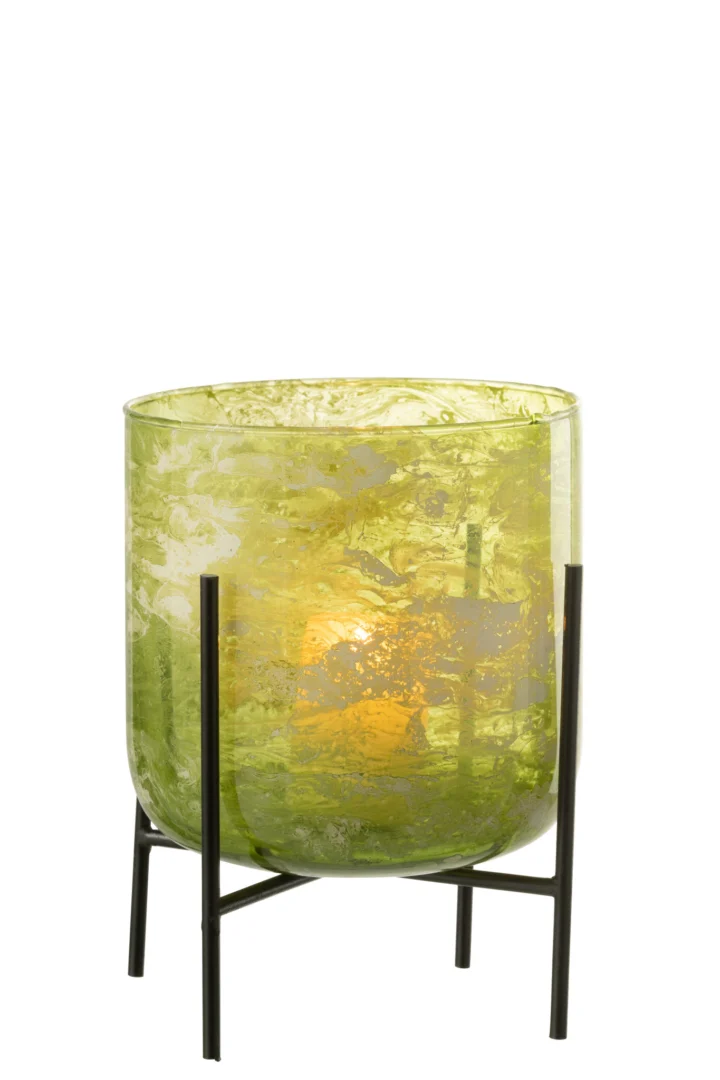 De Kaarsenhouder Orkaan Stand Glas Marmer Groen Groot is een groen gemarmerde glazen kandelaar met een brandende kaars erin, op een zwart metalen standaard met vier poten.