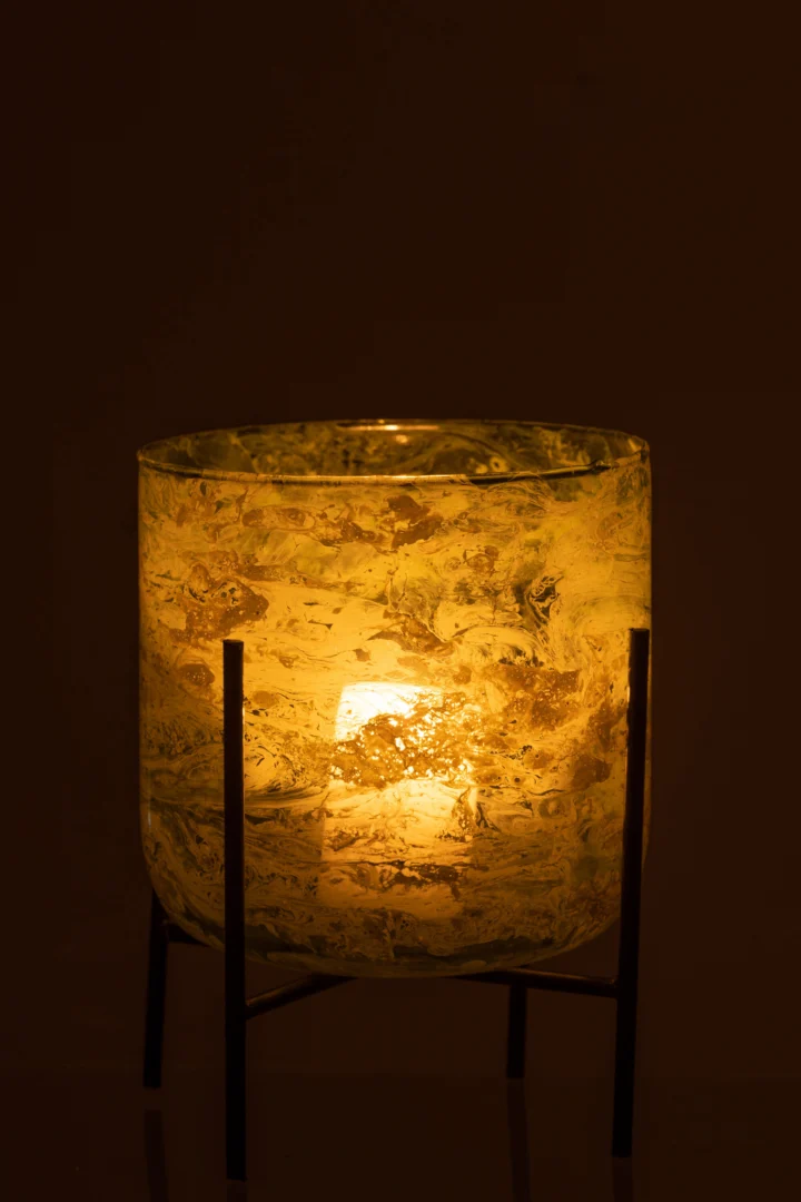 De Kaarsenhouder Orkaan Stand Glas Marmer Groen Groot heeft een brandende kaars die warm opgloeit in een houder van groen gestructureerd glas op een marmeren standaard die zachtgeel licht werpt tegen een donkere achtergrond.