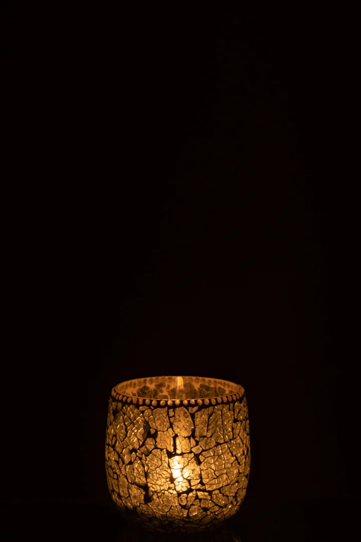 Het Theelichthouder Mozaïekglas Groen Wit Klein gloeit warm in het donker. Het decoratieve glas met mozaïekpatroon werpt een zacht licht tegen een zwarte achtergrond.