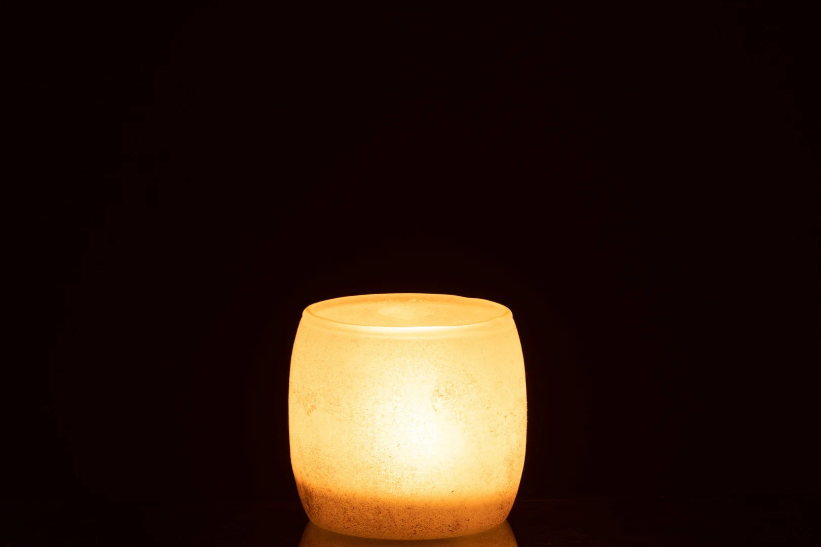 Een enkele Theelichthouder Poederglas Roze Klein gloeit warm in zijn matroze glazen houder tegen een donkere achtergrond.