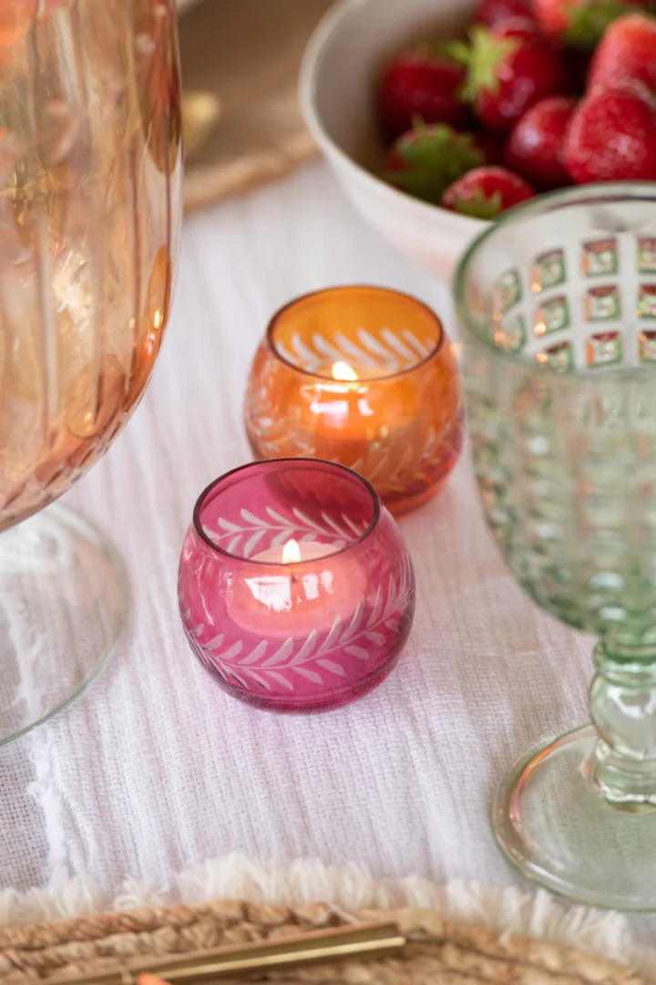 Een close-up van Theelichthouder Bladeren Glas Rond Mix Set van 3 waxinelichthouders op een wit tafelkleed, naast een groene glazen bokaal, een groot glas en een schaal met verse aardbeien.