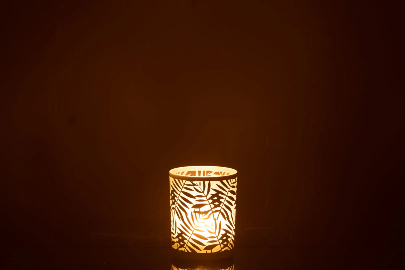 De Kaarsenhouder Orkaan Laat Glas Wit Medium heeft een ontwerp met bladmotief dat, wanneer verlicht, een warme gloed en elegante schaduwen werpt op een donkere achtergrond.