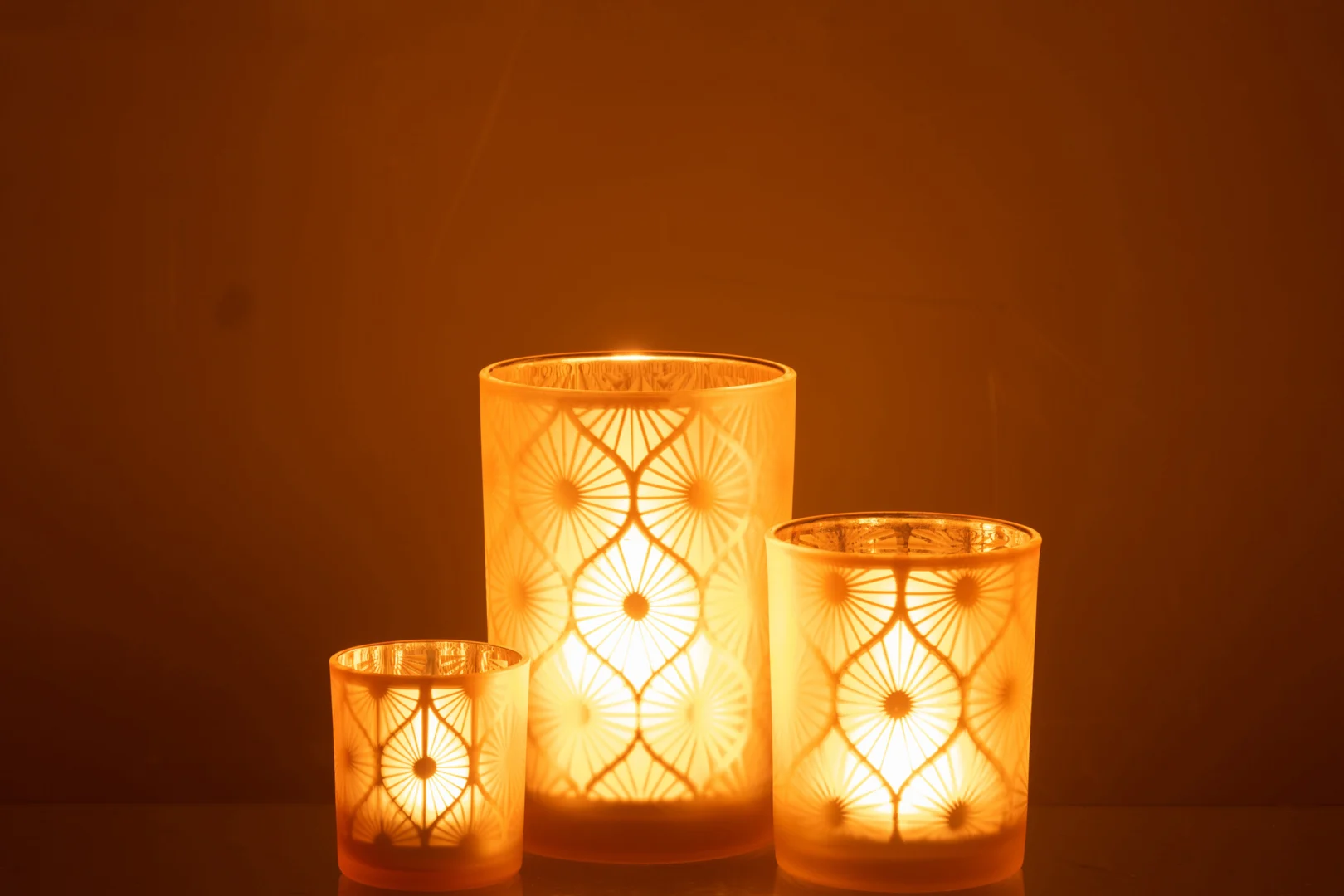 Een grote Kaarsenhouder Orkaan Rhomb Bloemen glazen kandelaar in geel, met geometrische en bloemmotieven, straalt warm tegen een donkere achtergrond.