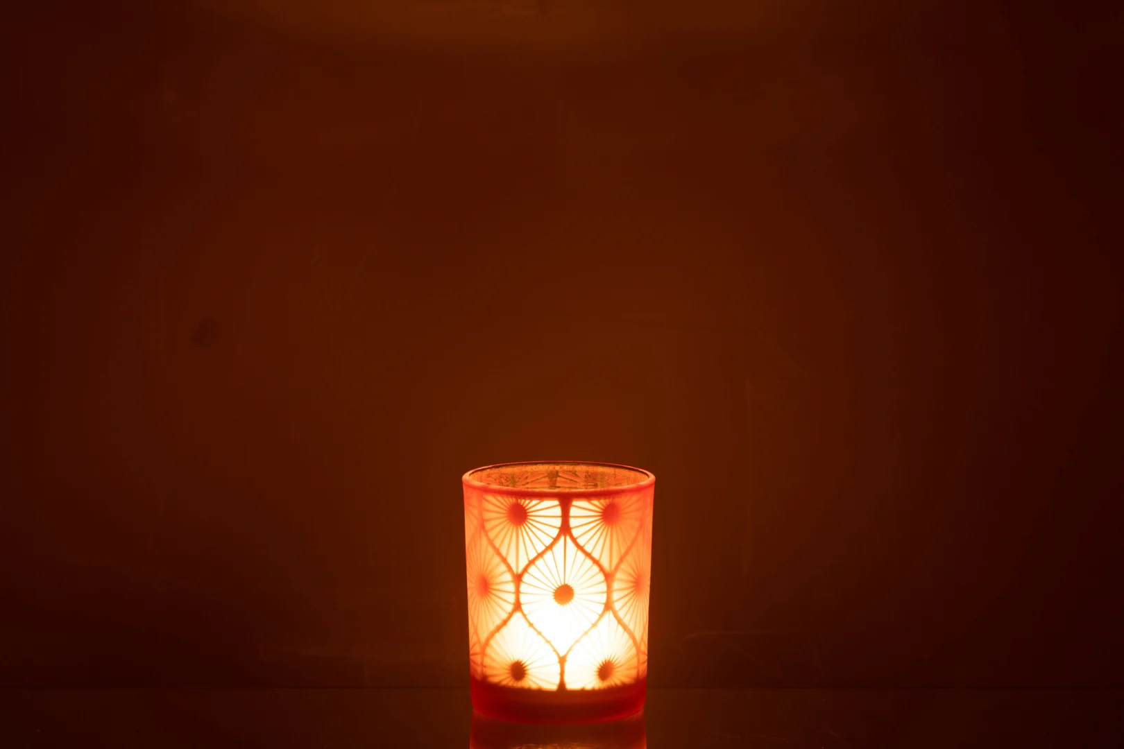 De Orkaan Rhomb Bloemen Glas Oranje Medium kaars gloeit warm in een decoratieve glazen houder, vult een donkere kamer met gezellig oranje licht en creëert een zachte, uitnodigende sfeer.