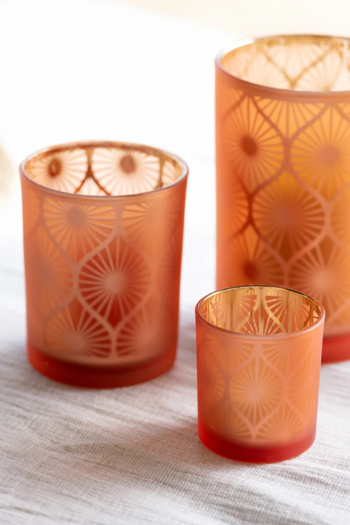 De Orkaan Rhomb Bloemen Glas Oranje Medium, met een oranje glazen body met een goudkleurig geometrisch patroon, wordt samen met zijn kleine en grote tegenhangers getoond op een lichtgekleurd gestructureerd oppervlak.