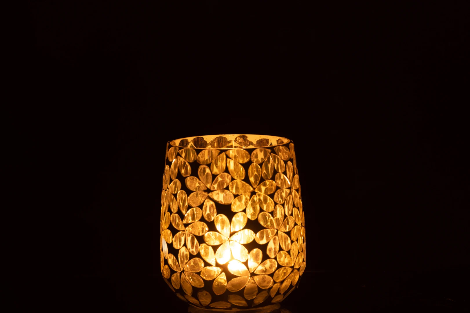 De Kaarsenhouder Orkaan Bloemen Glas Geel Zilver Middelgroot heeft een bloemmotief dat warm oplicht in het donker en elegante gouden schaduwen werpt.