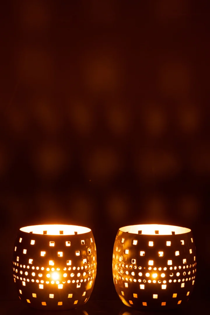 De Kaarsenhouder geperforeerd metaal groen assortiment van 2 werpt een warme gloed in het donker, met zijn decoratieve uitgesneden ontwerp dat zacht licht en geometrische schaduwen projecteert op nabijgelegen oppervlakken.