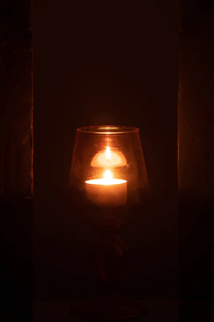 Een brandende kaars in de Kaarsenhouder Glas Roze Framboos Klein werpt een warme, zachte gloed door het roze glas en verlicht de duisternis.