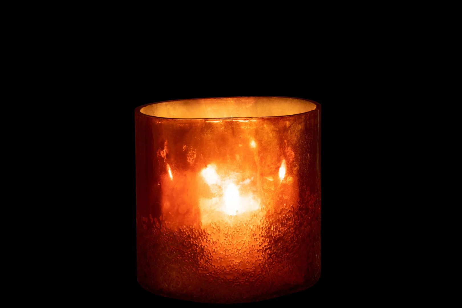 De Spiegel Goud Glas Extra Groot Formaat kaars gloeit warm in zijn oranje houder tegen een volledig zwarte achtergrond.