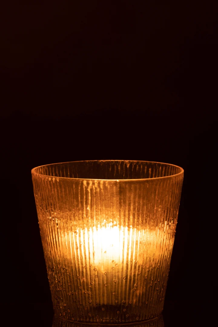 De Kaarsenhouder Orkaan Geribbeld Glas Roze Groot houdt een glimmende kaars vast, waarvan het geribbelde roze glas zacht, warm licht werpt in de duisternis.