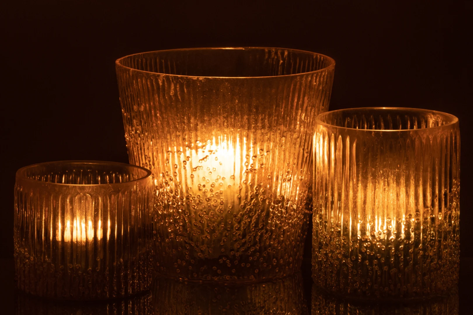 De Kaarsenhouder Orkaan Geribbeld Glas Roze Groot kandelaar gloeit warm met een brandende kaars erin. Het geribbelde glazen ontwerp creëert een gezellige en uitnodigende sfeer tegen een donkere achtergrond.