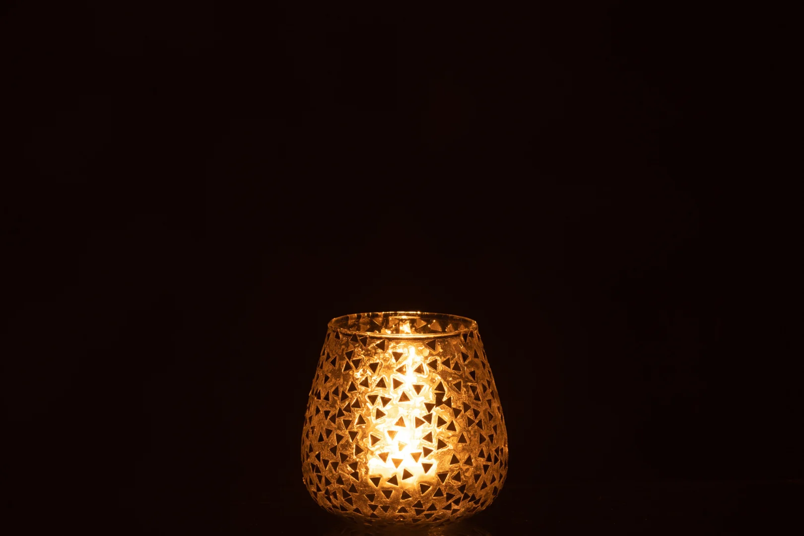De Kaarsenhouder Orkaan Driehoek Glas Goud Groot straalt warm in zijn decoratieve glazen houder, met ingewikkelde uitsnijdingen die een zachte, flikkerende gloed creëren tegen een donkere achtergrond.
