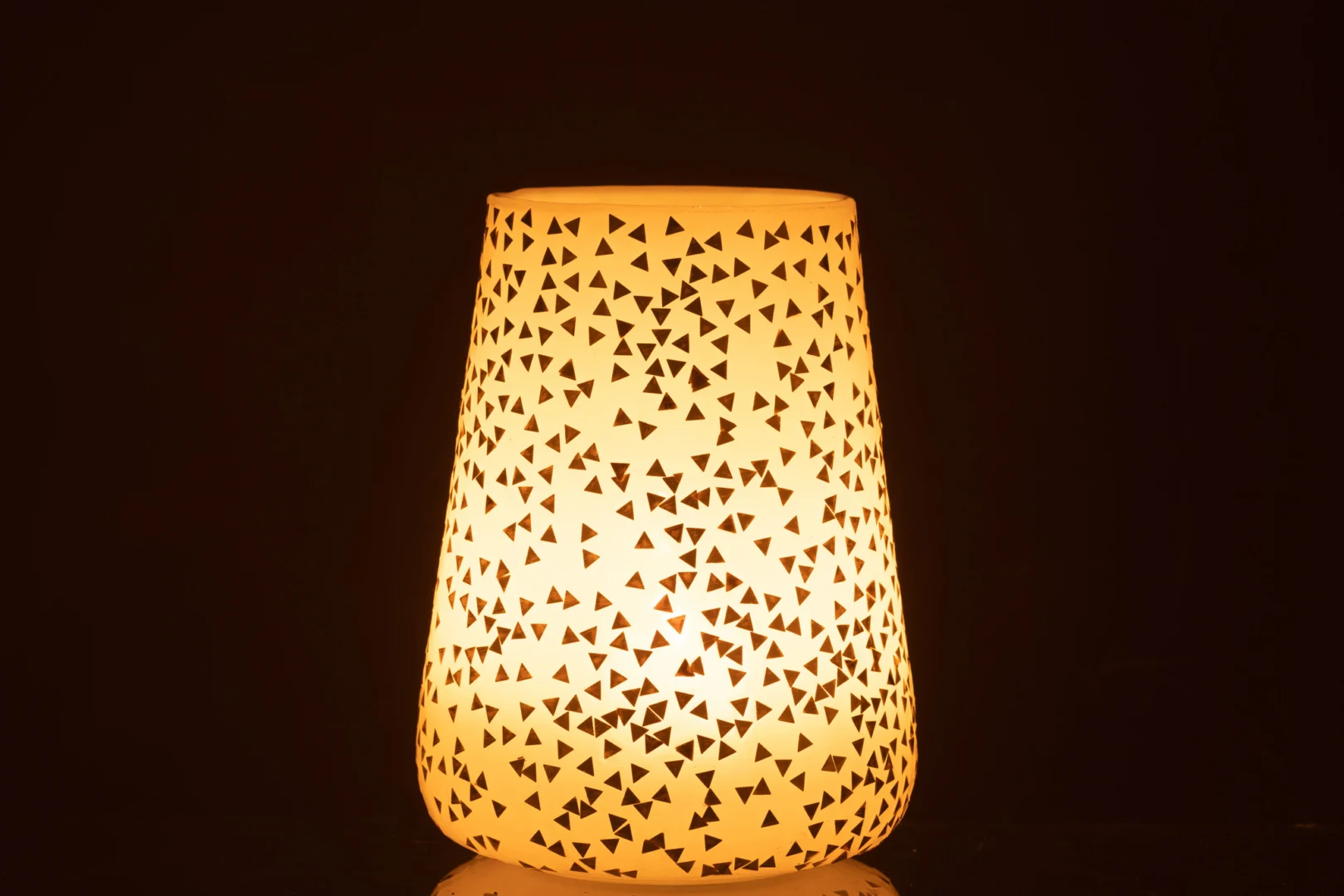 De Kaarsenhouder Orkaan Driehoek Glas Wit Goud Extra Groot heeft een crèmekleurige kap met onregelmatige driehoekige uitsparingen, die decoratieve lichtpatronen werpt tegen een donkere achtergrond.