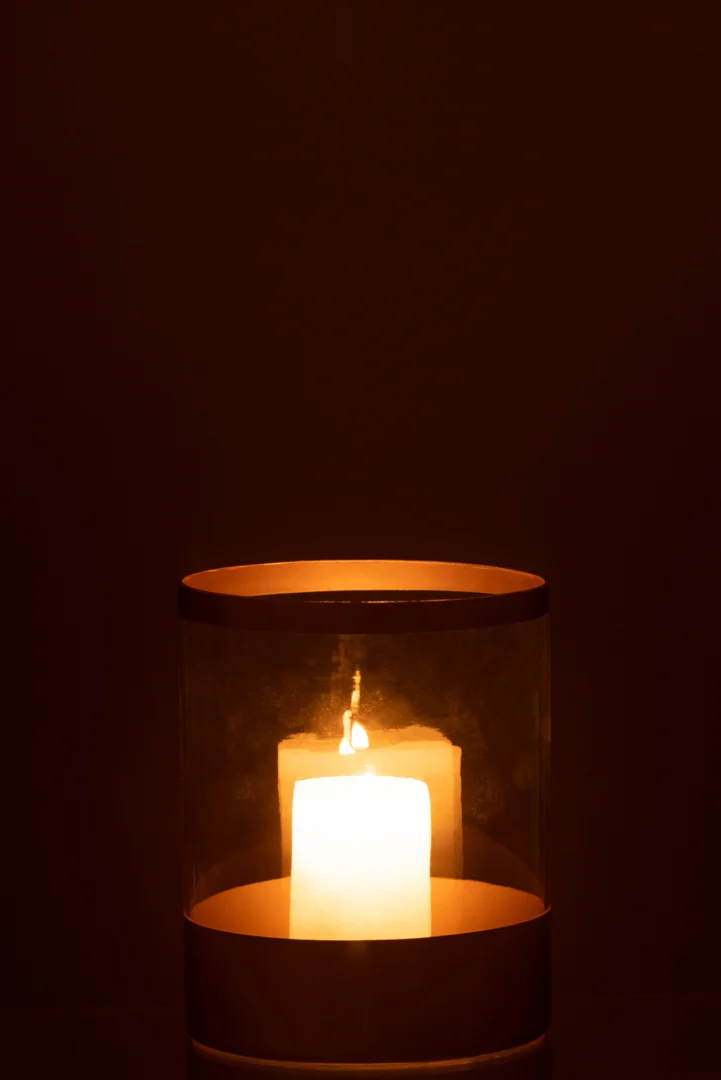 Een enkele kaars gloeit warm in de Kaarsenhouder Orkaan Gouden Lijnen Glas Groot, het heldere glas en de gouden lijnen werpen zacht licht tegen een donkerbruine achtergrond.