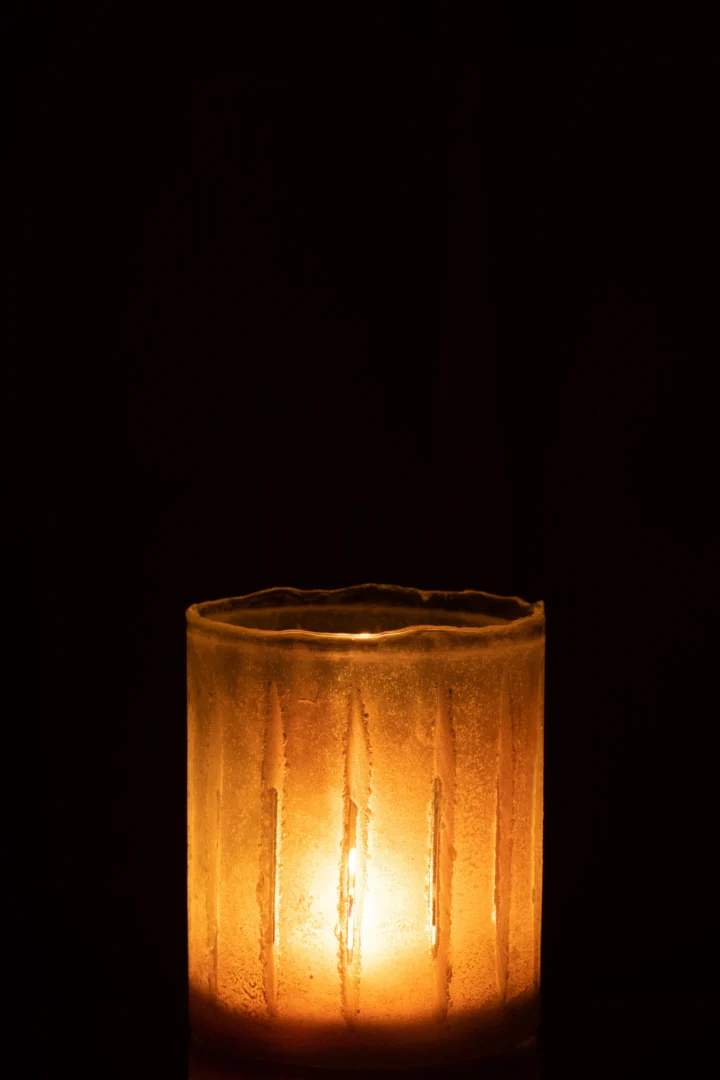 De Kaarsenhouder Strepen Glas Geel Klein gloeit warm in de duisternis, de gele glazen houder werpt een zacht, gezellig licht en creëert een uitnodigende sfeer.