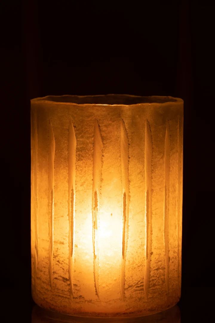 De Kaarsenhouder Strepen Glas Geel Groot heeft een brandende kaars in een matte, verticaal gegroefde glazen houder, die een zachte amberkleurige gloed in het donker werpt.