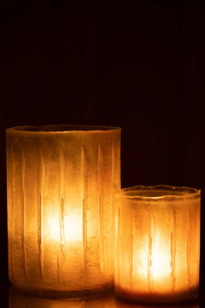 Een grote geel gestreepte glazen kandelaar, Kaarsenhouder Strepen Glas Geel Groot, straalt warm tegen een donkere achtergrond en creëert een gezellige en serene sfeer.