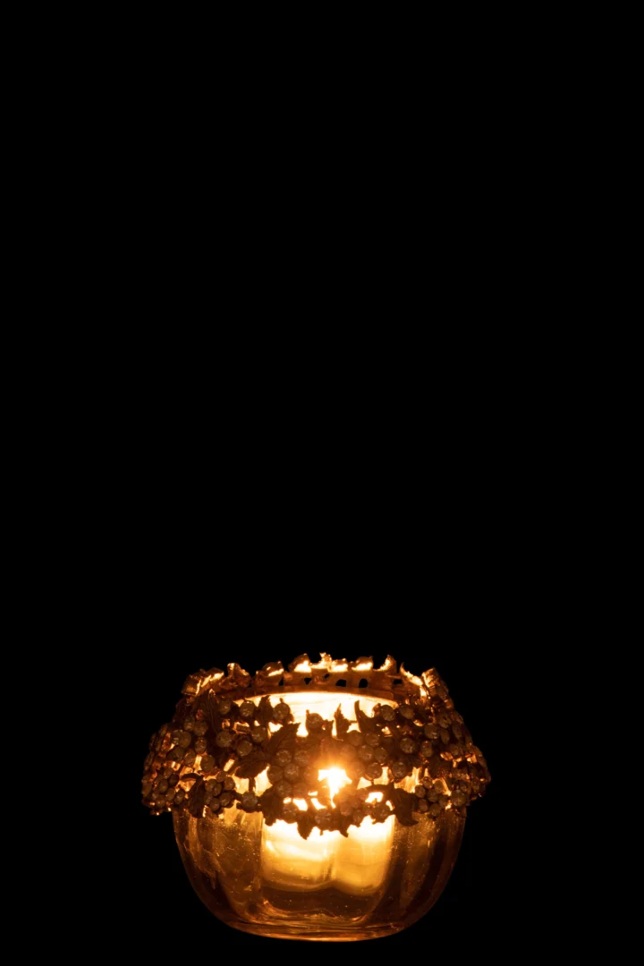 De Theelichthouder Volve Metaal Glas Goud Brons Klein kandelaar gloeit warm, één brandende kaars verlicht het decoratieve goudbronzen glas tegen een diepzwarte achtergrond.