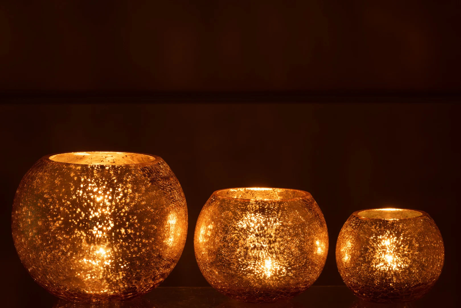 De Theelichthouder Orkaan Craquelure Glas Goud Groot gloeit warm, werpt een zacht, gespikkeld licht in donkere omgevingen en creëert een gezellige, uitnodigende sfeer met zijn prachtige gouden glazen ontwerp.