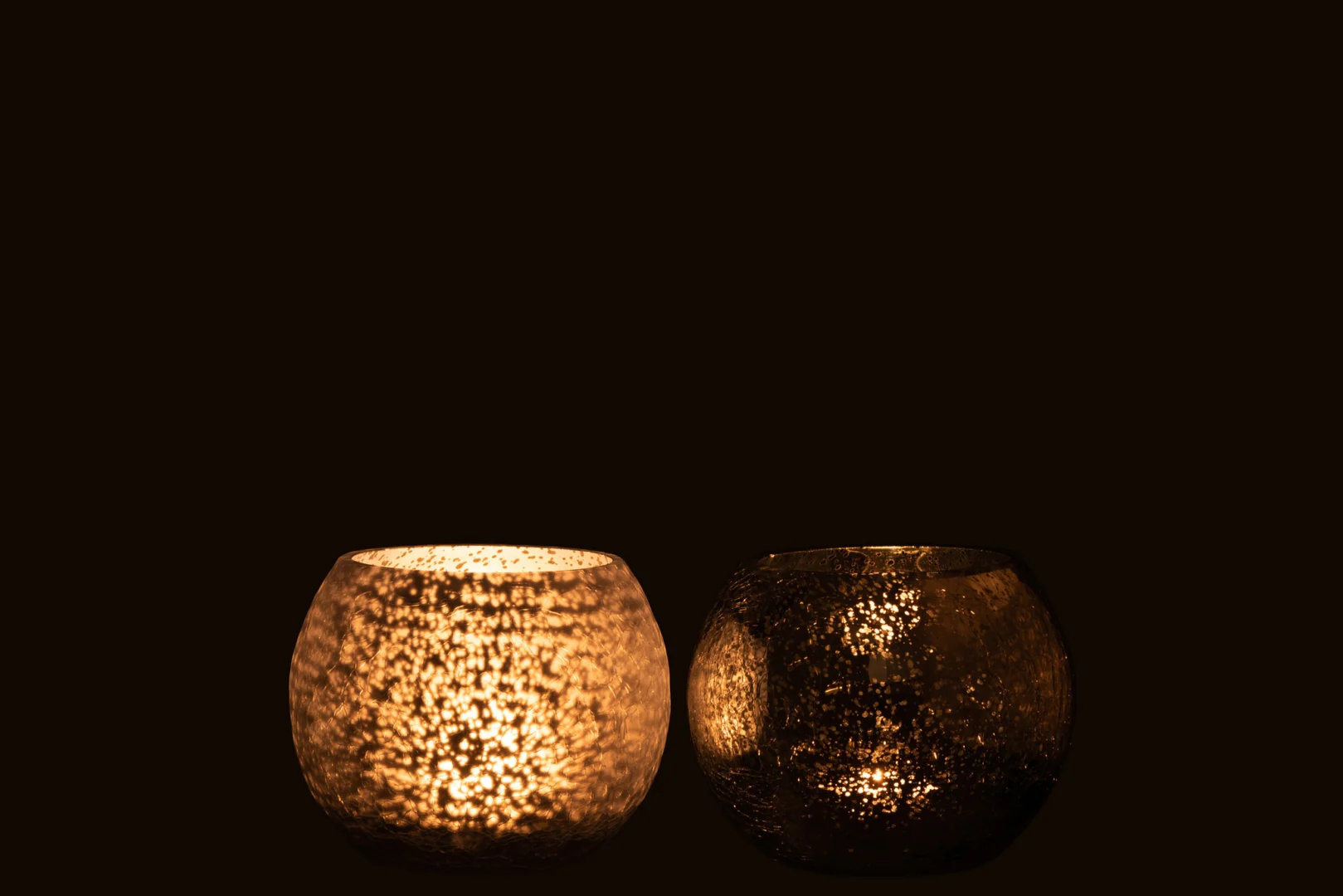 Twee Theelichthouder Sphere Craquelure Glas Blauw Klein kandelaars zitten naast elkaar tegen een zwarte achtergrond; de linker gloeit warm, terwijl de rechter onverlicht en donker blijft. Set van 2.