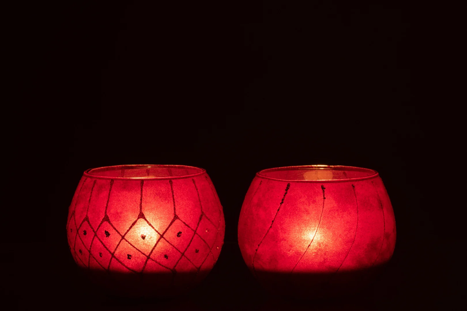 De Kaarsenhouder Hurricane Velvet Glas Rood Goud Set 2 heeft twee ronde rode kandelaars met gouden accenten, die zacht gloeien tegen een donkere achtergrond en een warme, gezellige sfeer creëren.