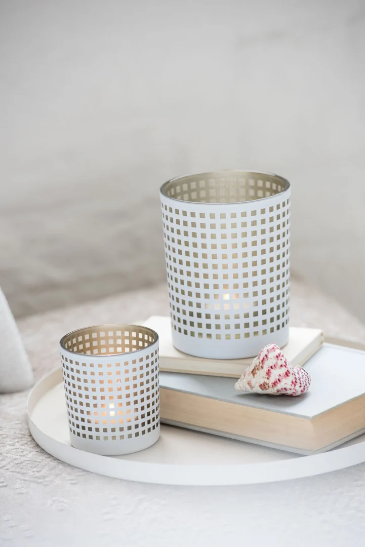 Een wit dienblad toont Theelichthouder Patroon Glas Wit Beige Set 2, een schelp en twee gesloten boeken op een licht stoffen oppervlak.