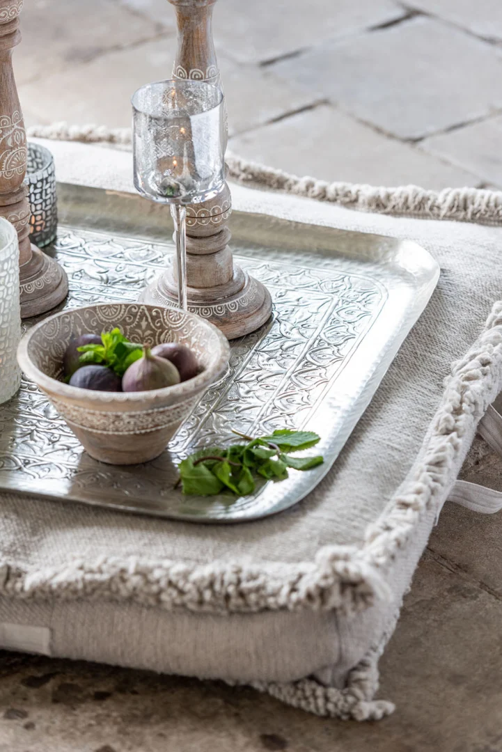Op een zilveren dienblad met ingewikkelde patronen staan de Theelichthouder Op Voet Oosters Glas Zilver Groot, een glas, een schaaltje vijgen en verse munt. Het dienblad staat op een kussen met textuur en kwastjes op een stenen vloer.
