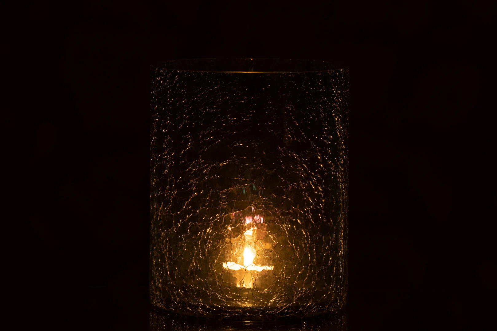De Kaarsenhouder Orkaan Crackle Glas Groen Groot werpt een zachte, warme gloed door het groen getextureerde glas en creëert subtiele reflecties en sfeer tegen een donkere achtergrond.