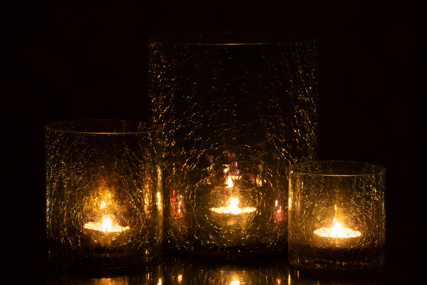 De Kaarsenhouder Orkaan Crackle Glas Groen Groot gloeit warm in het donker en werpt een zacht gouden licht en reflecties op het gebarsten groene glas en de omgeving.