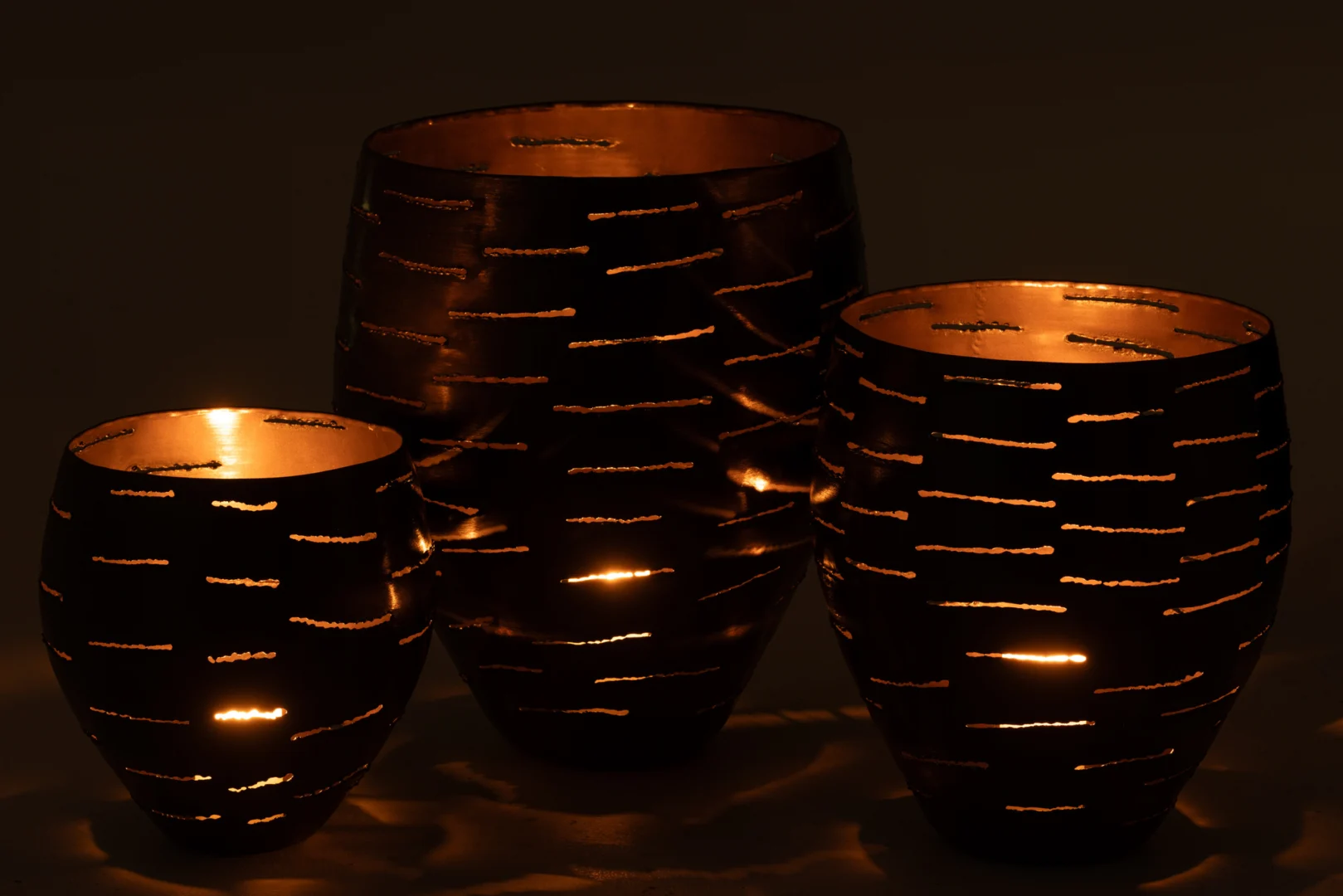 De Set van 3 Orkaan schalen Metaal Zwart - Kaarsenhouders stralen een warme gloed uit door hun uitsparingen en werpen prachtige patronen van licht en schaduw in het donker.