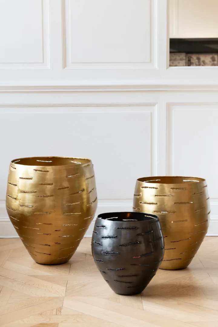 De Set van 3 Orkaankommen Metaal Zwart - Kaarsenhouders bestaat uit drie decoratieve metalen kommen met een getextureerde afwerking, elegant gepresenteerd op een lichte houten vloer voor wit gelambriseerde muren.