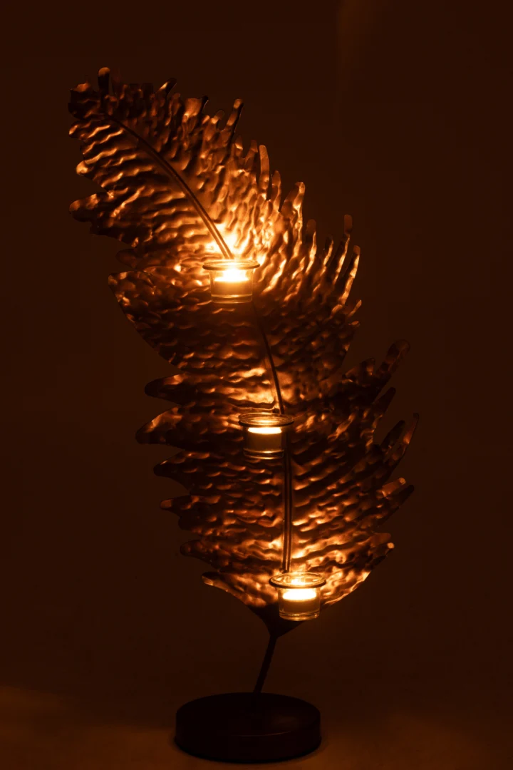 De Kaarsenhouder Blad Metaal Glas Bruin is een decoratieve metalen bladvormige kandelaar waar drie waxinelichtjes in passen en die een warme gouden gloed creëert in schemerig licht.