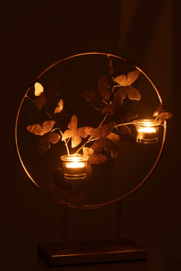 De Kaarsenhouder Vlieg Metaal Goud is een ronde metalen kandelaar met vlindermotieven. Hij houdt twee waxinelichtjes vast die een warme, gouden gloed in het donker werpen.