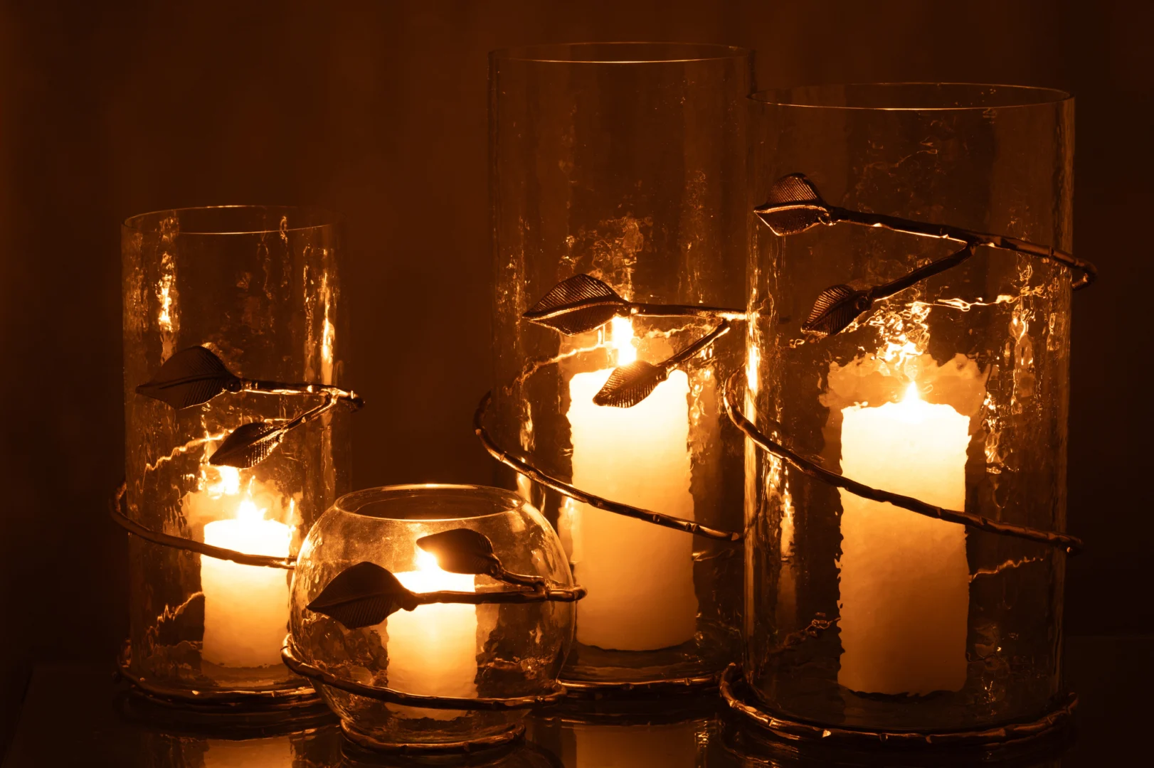 Drie Vaas Blad Kom Glas IJzer Transparant Goud vazen van verschillende hoogtes, elk omwikkeld met goudkleurige metalen ranken en bladeren, stralen warm in een donkere, sfeervolle omgeving.