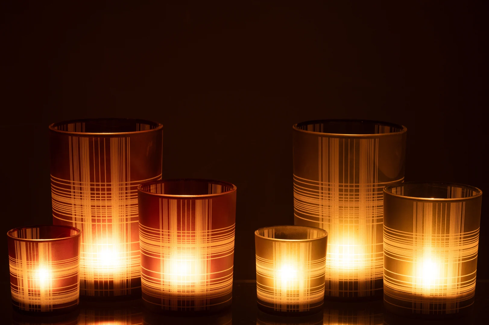 De Kaarsenhouder Orkaan Controle Glas Bruin Groen Groot Set 2 heeft twee grote glazen kandelaars in bruin en groen, die een warme gloed werpen en een gezellige sfeer creëren tegen een donkere achtergrond.