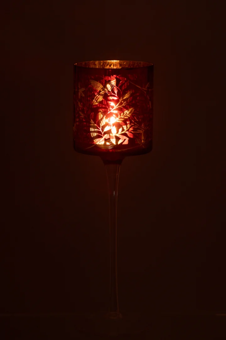 Theelichthouder Op Voet Bladeren Glas Rood/Antiek Goud Groot gloeit warm in het donker, met een rode glazen kap met bladmotieven op een slanke, transparante standaard.