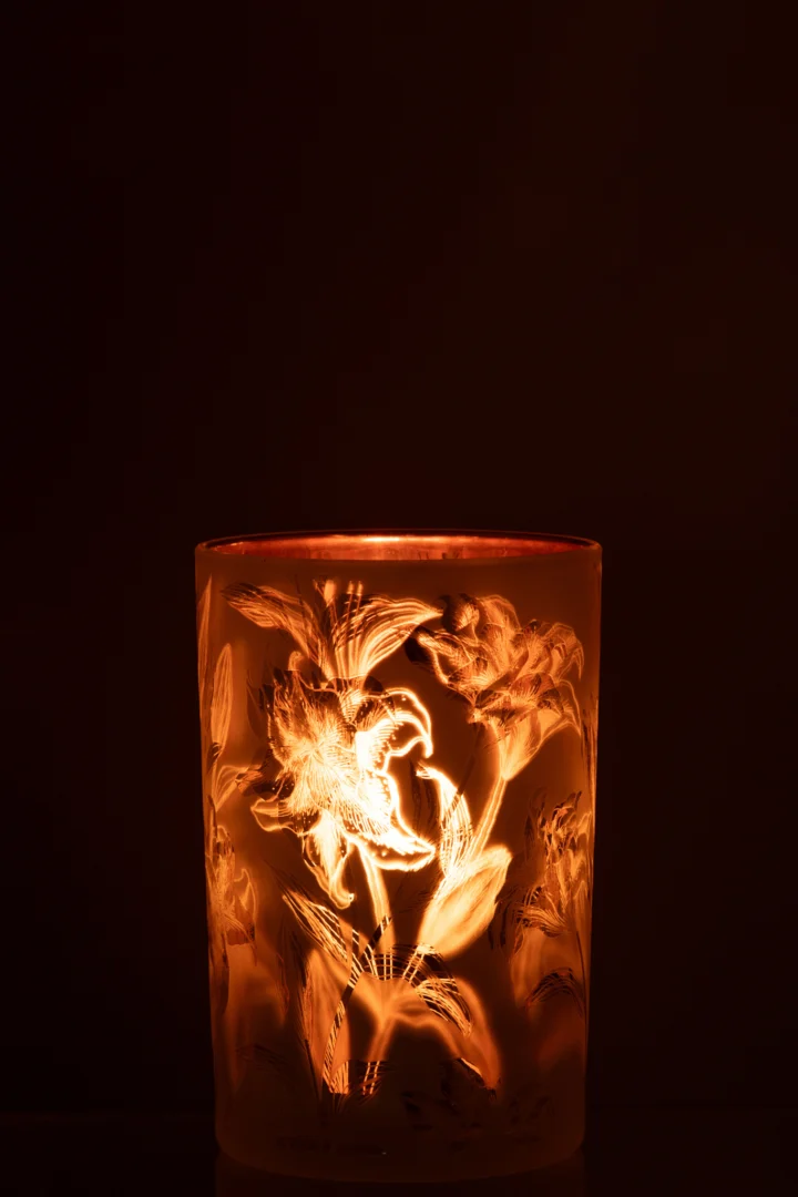 De Kaarsenhouder Orkaan Bloemen Glasmat Wit Rood Goud Groot heeft een gloeiende kaars in een matglazen houder met bloemmotieven, die warm, zacht licht werpt tegen een donkere achtergrond.