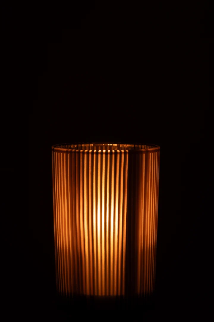 De Kaarsenhouder Orkaan Strepen Glas Bruin Wit Groot straalt warm en werpt goudkleurig licht van het geribbelde glazen ontwerp tegen een donkere achtergrond.