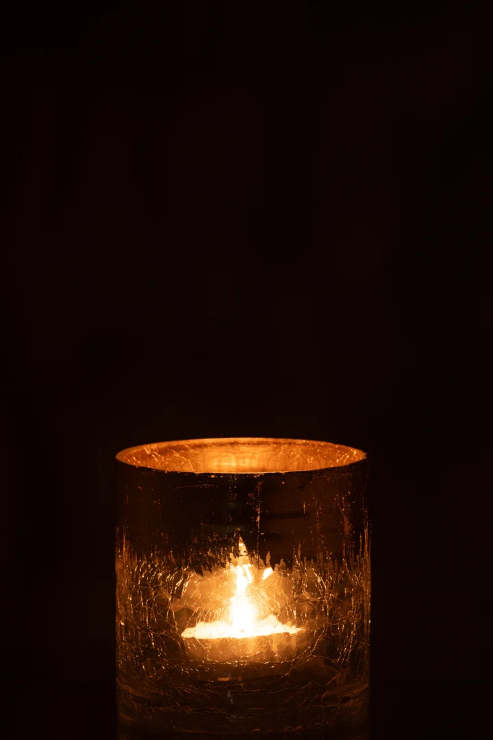 De Kaarsenhouder Orkaan Crackle Glas Transparant Goud Medium werpt een zachte, gouden gloed door het getextureerde glas en verlicht de duisternis zachtjes met warm kaarslicht.