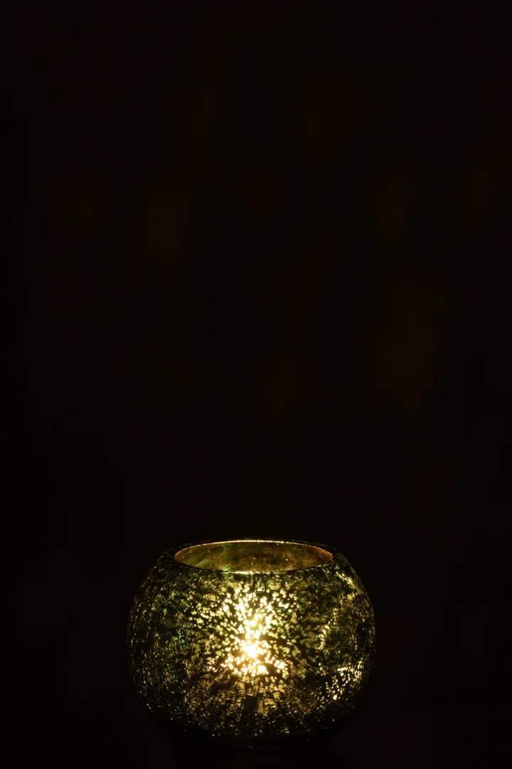 De Theelichthouder Bal Craquelure Glas Watergroen Klein is een kleine, ronde glazen kandelaar met textuur en een brandende kaars erin, die een warme gouden gloed in het donker werpt.