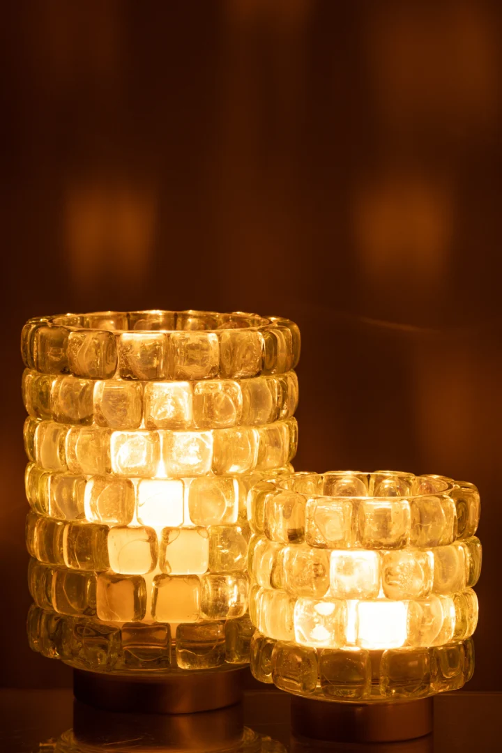 De Kaarsenhouder Orkaan Vierkant Mozaïekglas Transparant Groot gloeit warm met een brandende kaars erin, werpt een zacht gouden licht en reflecties op de omringende oppervlakken.