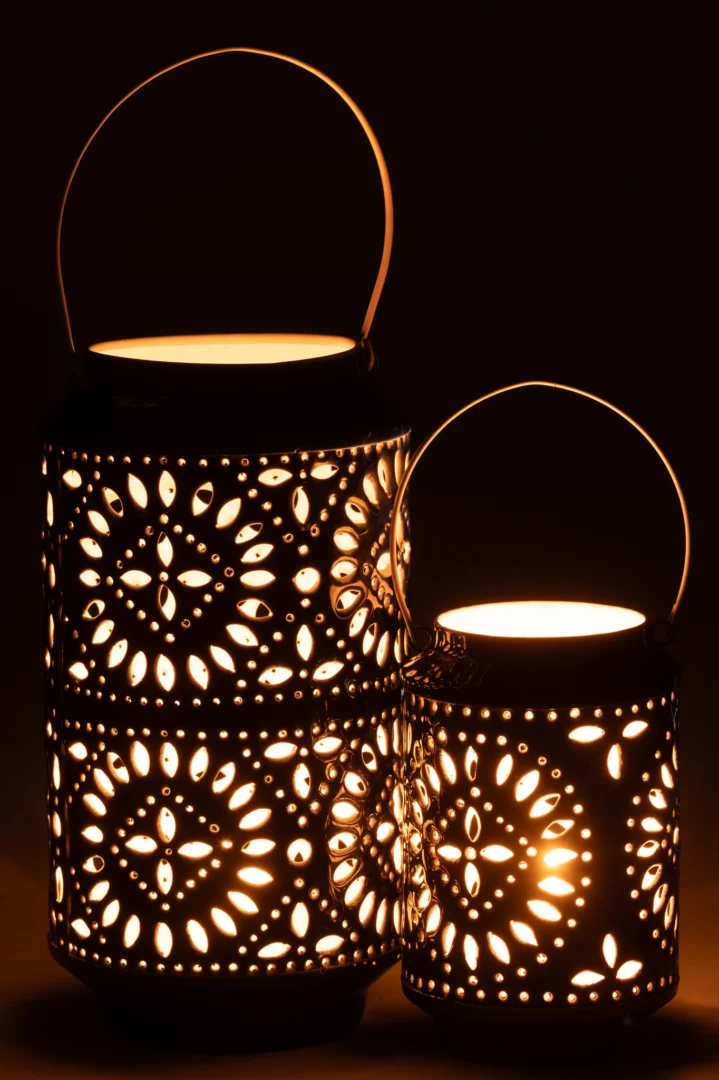 Twee Kaarsenhouder Orkaan Nag IJzer Blauw Wit Groot lantaarns met ingewikkelde uitgesneden patronen gloeien warm op in het donker. De lange lantaarn staat achter en links van de korte en beide hebben gebogen handvatten.