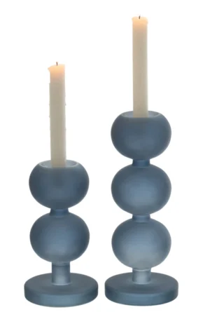Twee witte kaarsen zitten in de Kaarsenhouder Malik Glas Blauw Set 2-moderne matblauwe houders met gestapelde bollen en ronde voet, waarvan er één een kortere kaars vasthoudt. De achtergrond is wit.