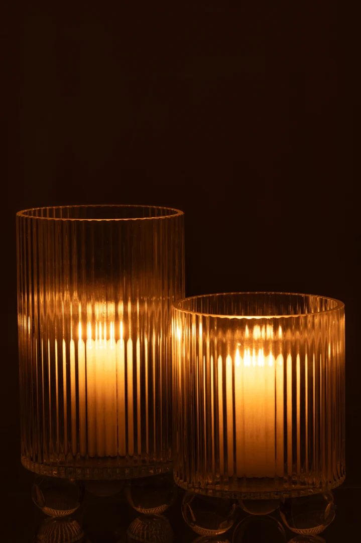 Twee Orkaan Clara Glas Transparant Groot kaarsenhouders, die elk een brandende kaars vasthouden, staan naast elkaar tegen een donkere achtergrond en werpen een warme en zachte gloed.