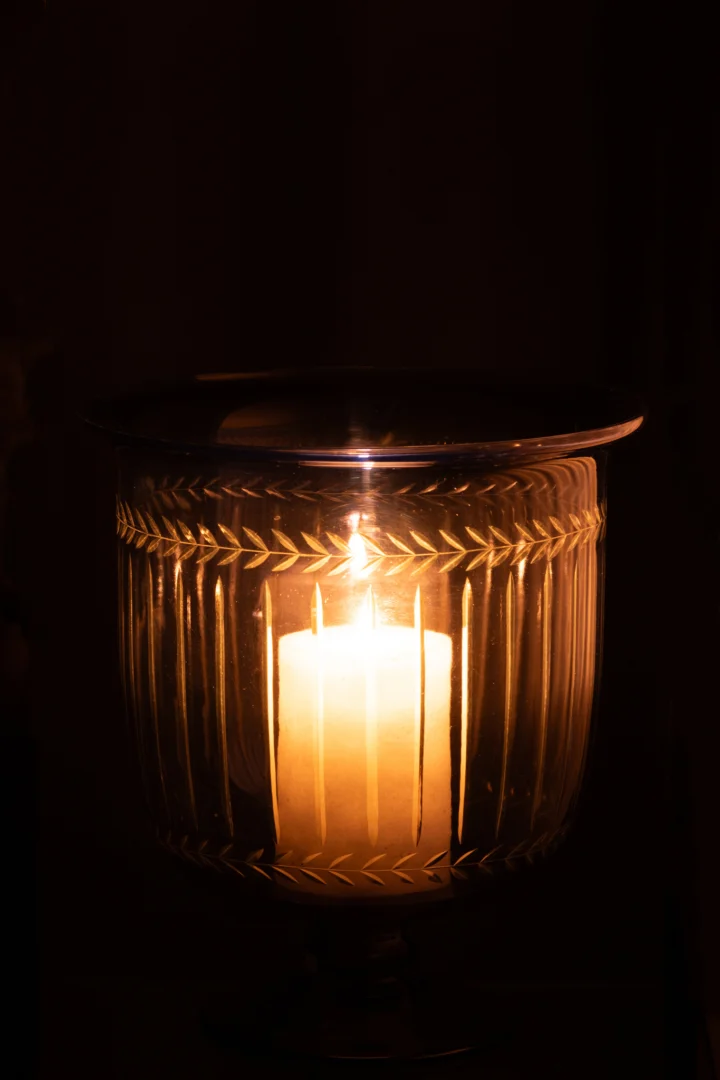 De Orkaan/Vaas Tarifa Glas Blauw - Kaarsenhouder houdt een brandende witte kaars binnen in het transparante, blauw gestructureerde glas, dat een warme gloed in het donker werpt.